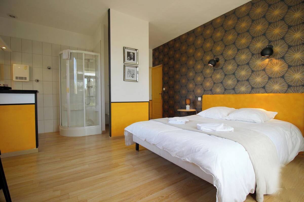 A hotel room with a bed, a shower, a vanity, and a patterned wall.