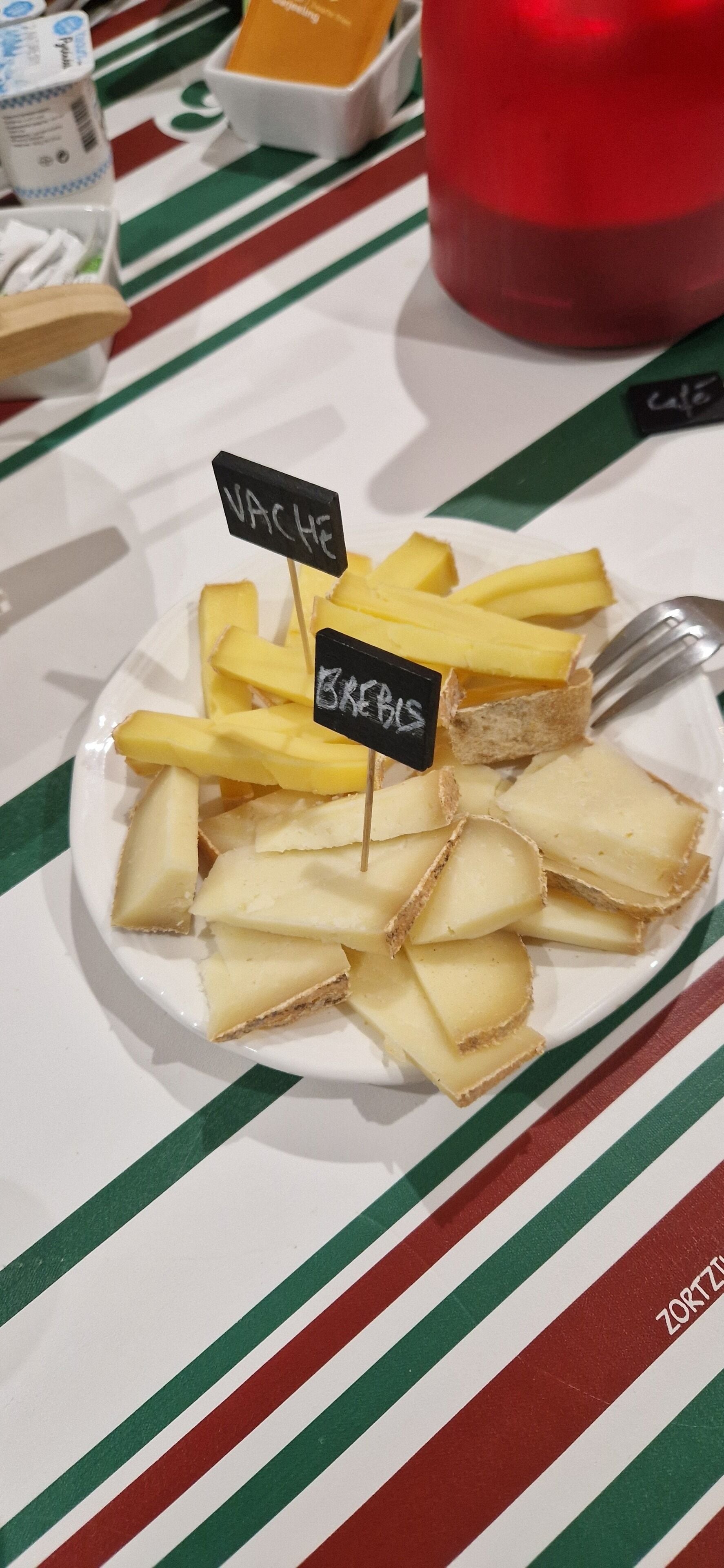 Ein Teller mit Käse und Crackern, beschriftet mit 'VACHE' und 'BEBE', auf einer gestreiften Tischdecke.