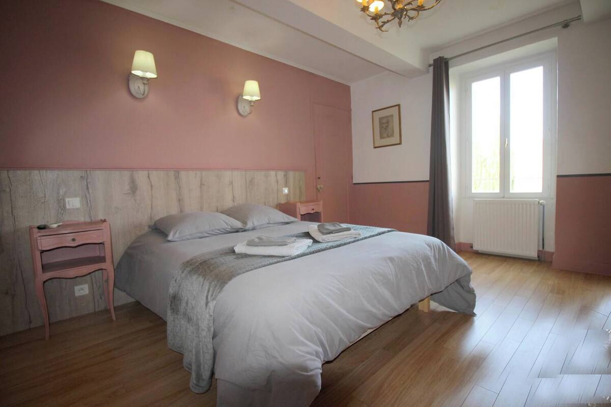 A bedroom with a bed, bedside tables, a radiator, and a window with curtains.
