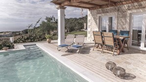 Un espace aménagé au bord de la piscine, comprenant une pergola, des chaises longues et une table avec des chaises.
