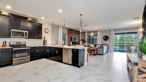 Una cocina moderna con armarios oscuros, electrodomésticos de acero inoxidable y piso de mármol.