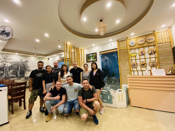 Un grupo de personas en una sala bien iluminada con un diseño de techo moderno, una recepción con objetos decorativos y una pared con un mural y una pantalla de bambú.