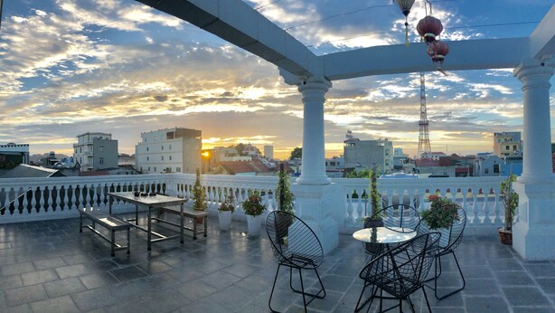 A rooftop terrace with a table and chairs, potted plants, and a view of the sunset over a cityscape. - O Zoli Home (Ninh Binh)