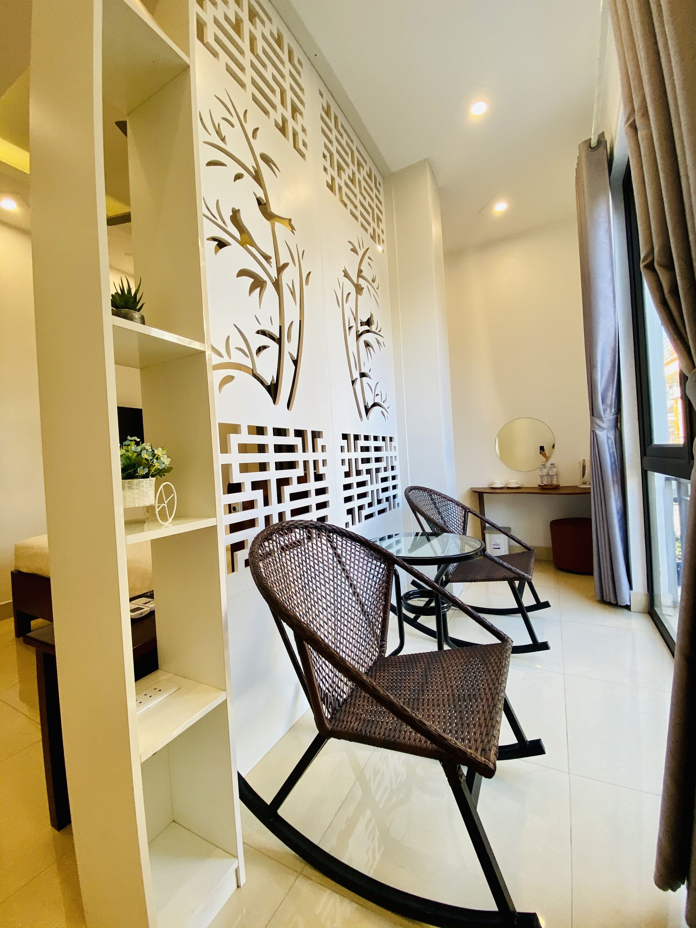 Una sala de estar moderna con una mesa de comedor de vidrio, dos mecedoras de mimbre, un panel decorativo y una mesita de noche con lámpara.