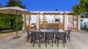 Un patio al aire libre con suelo de piedra, una sombrilla grande y una mesa de madera con sillas.