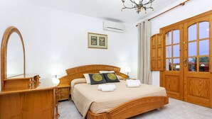 Habitación de hotel con cama de madera, un espejo grande, una mesita de noche con lámpara, un armario y una ventana con cortinas.