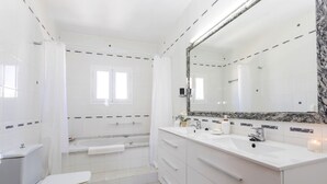 Un baño moderno con inodoro blanco, bañera, un espejo grande con marco de mármol y tocador con lavamanos y encimera.
