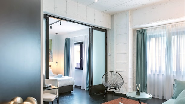 Une chambre d’hôtel comprenant un lit, un coin salon avec une chaise et une table, et une vue sur l’extérieur à travers les rideaux.