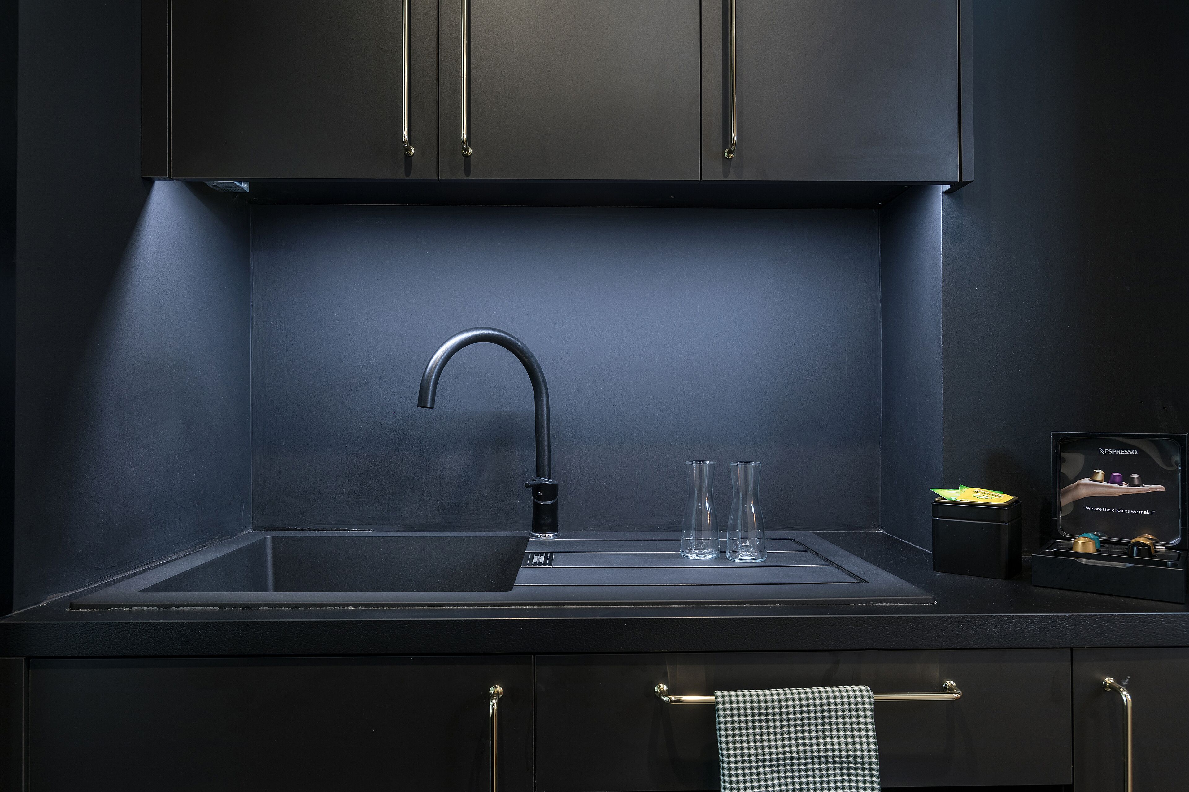 Une cuisine moderne dotée d’un élégant plan de travail noir, d’un unique robinet et d’une machine à café Nespresso.