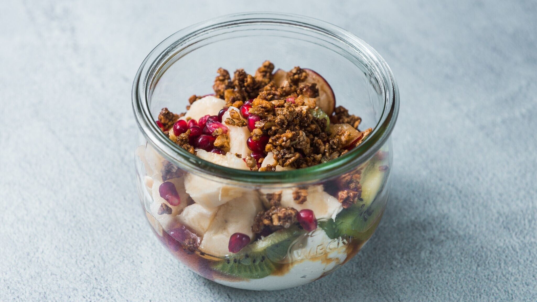 A glass jar containing a layered dessert with fruits and granola.