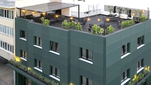 Un bâtiment moderne doté d’une terrasse sur le toit, aménagée avec des espaces de détente en plein air et des plantes.