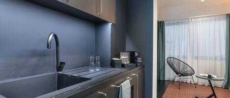 A compact kitchen with a modern sink, a small countertop, and a chair near a window.