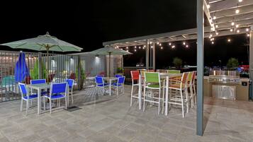 An outdoor patio area with tables and chairs, string lights, and umbrellas.