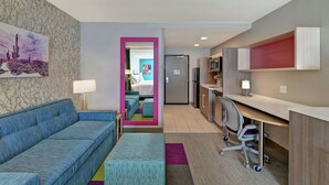 Une chambre d’hôtel équipée d’un canapé, d’un bureau, d’une chaise, d’un lit et d’un coin cuisine.