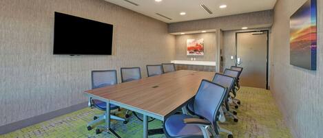 A conference room with a large table, chairs, a flat-screen TV, artwork on the walls, and a carpeted floor.