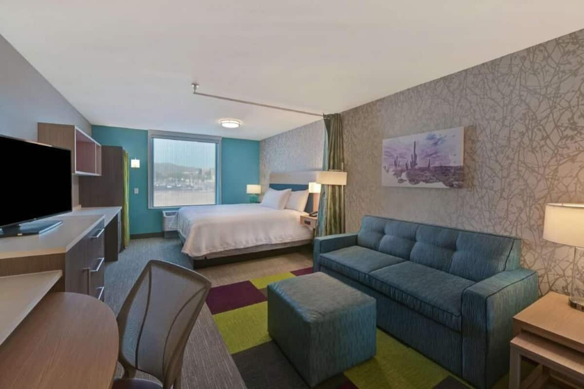 A hotel room with a bed, a sofa, a desk with a TV, and a window with a view.