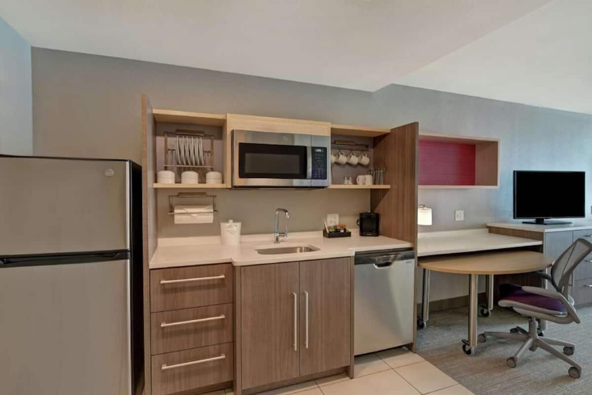 A compact kitchen with a microwave, sink, and a small dining area with a chair.