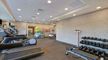 Un gimnasio con cintas de correr, una bicicleta estática y un banco para press de banca.