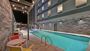 Une piscine bordée d’un mur en pierre, avec un immeuble à plusieurs étages en arrière-plan.