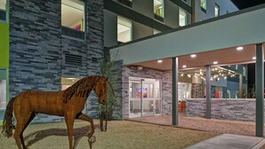 Un bâtiment moderne avec une façade en pierre, une entrée en verre et une grande statue de cheval en premier plan.