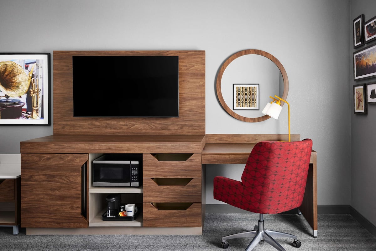 Un espacio de oficina moderno con un escritorio de madera, un televisor de pantalla plana, una silla de oficina roja, una cafetera y un cuadro enmarcado en la pared.