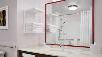 Un baño moderno con un espejo grande, toallas blancas, una ducha y un lavamanos con dispensador de jabón.