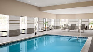 A swimming pool with a tiled deck, seating area with chairs and tables, and large windows with a view of the outdoors. - Hampton Inn & Suites Charlotte Steele Creek (Charlotte)