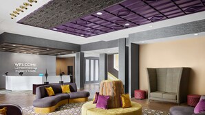 A modern lobby with a curved sofa, a round ottoman, and a reception desk with a 'WELCOME' sign. - Hampton Inn & Suites Charlotte Steele Creek (Charlotte)