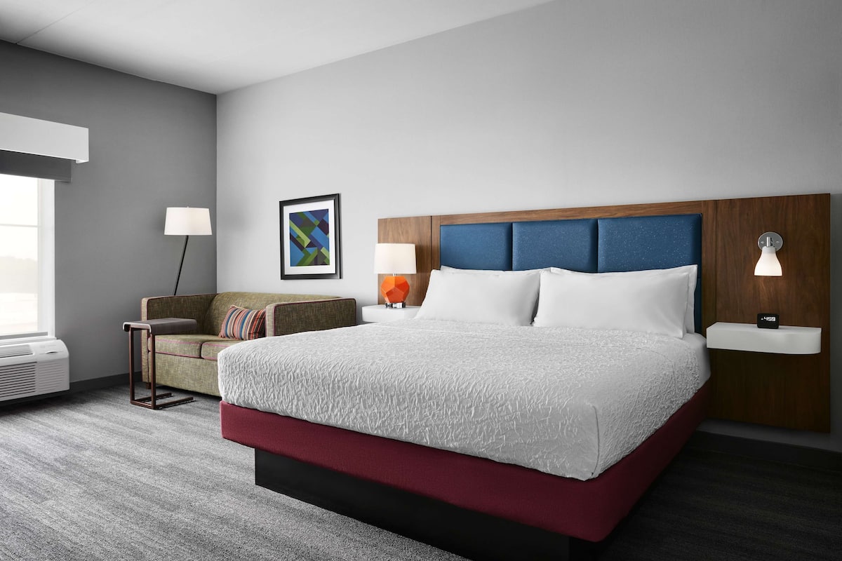 Una habitación de hotel con una cama grande, un sofá, una lámpara, un cuadro en la pared y una mesita de noche.