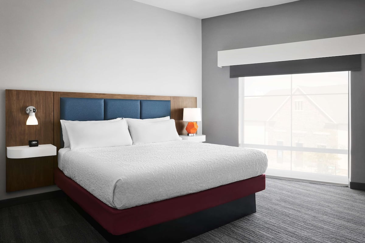 Habitación de hotel con una cama grande, dos mesitas de noche, una lámpara auxiliar y un ventanal con vistas, además de un cabecero moderno.