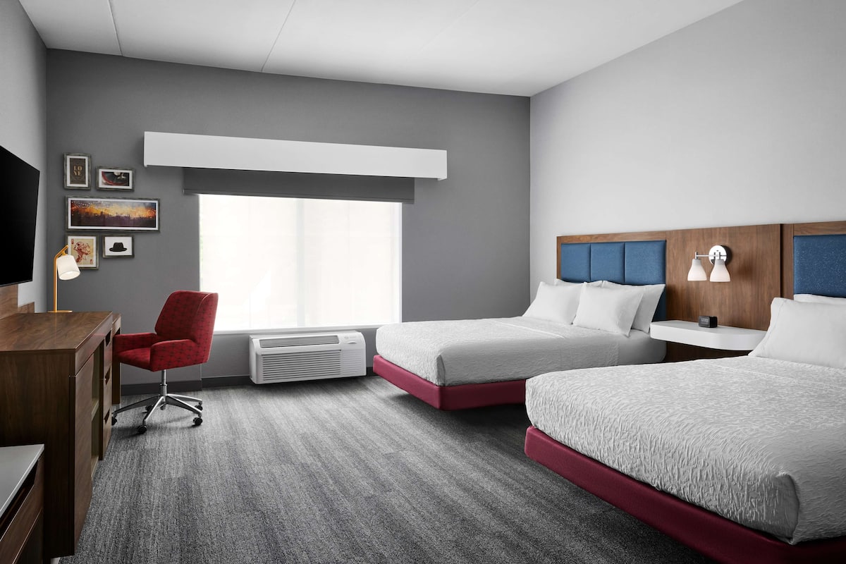 Habitación de hotel con dos camas, un escritorio, una silla, un televisor y una ventana con persianas.