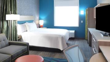 A hotel room with a bed, a desk, a chair, a sofa, and a television.
