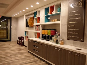 Un hall d’hôtel moderne avec un comptoir d’accueil, un espace café et un panneau indiquant une garantie de satisfaction.