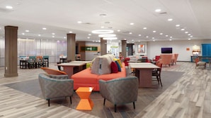 Un vestíbulo espacioso con diseño moderno, que incluye una zona de estar central con sofás y sillones, una mesita de centro y un mostrador de recepción.
