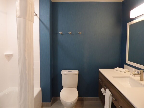 A bathroom with a white toilet, a bathtub, a sink with a mirror, and a towel rack. - Home2 Suites by Hilton Pensacola I 10 Pine Forest Road (Pensacola)