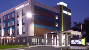 Un hotel con diseño moderno, que presenta un letrero llamativo para "HOME2 SUITES BY MILTON" y una entrada bien iluminada.