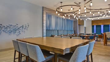 A modern conference room with a large wooden table, grey upholstered chairs, and a unique ceiling light fixture.