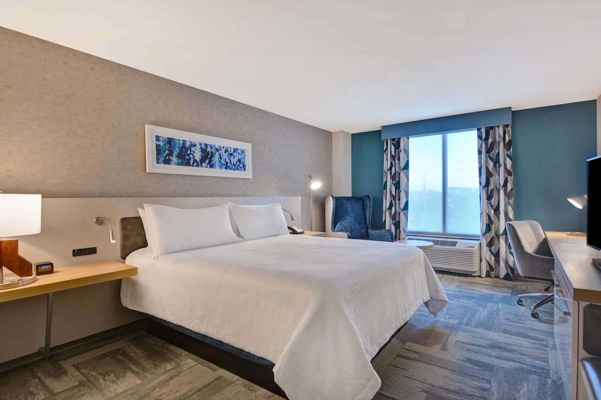 Una camera d'albergo con un letto grande, una scrivania con una lampada, una sedia e una televisione.