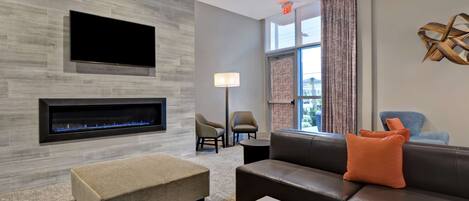 A modern living room with a fireplace, comfortable seating, a flat-screen TV, and a large window with curtains.