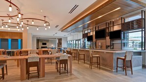 Ein modernes Restaurant mit Holztischen und -stühlen, einer Bar und großen Fenstern, die natürliches Licht hereinlassen.
