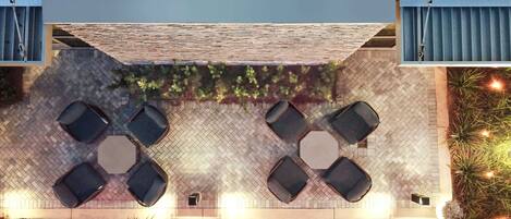 An outdoor seating area with hexagonal tables and chairs, surrounded by potted plants and decorative lights.