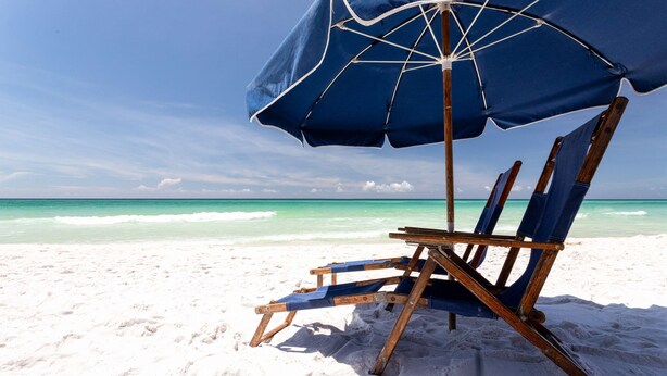 Ein Strandstuhl mit blauem Sonnenschirm am sandigen Strand.