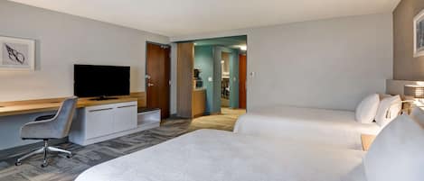 Habitación de hotel con dos camas, un escritorio con silla, un televisor y una cafetera al fondo.