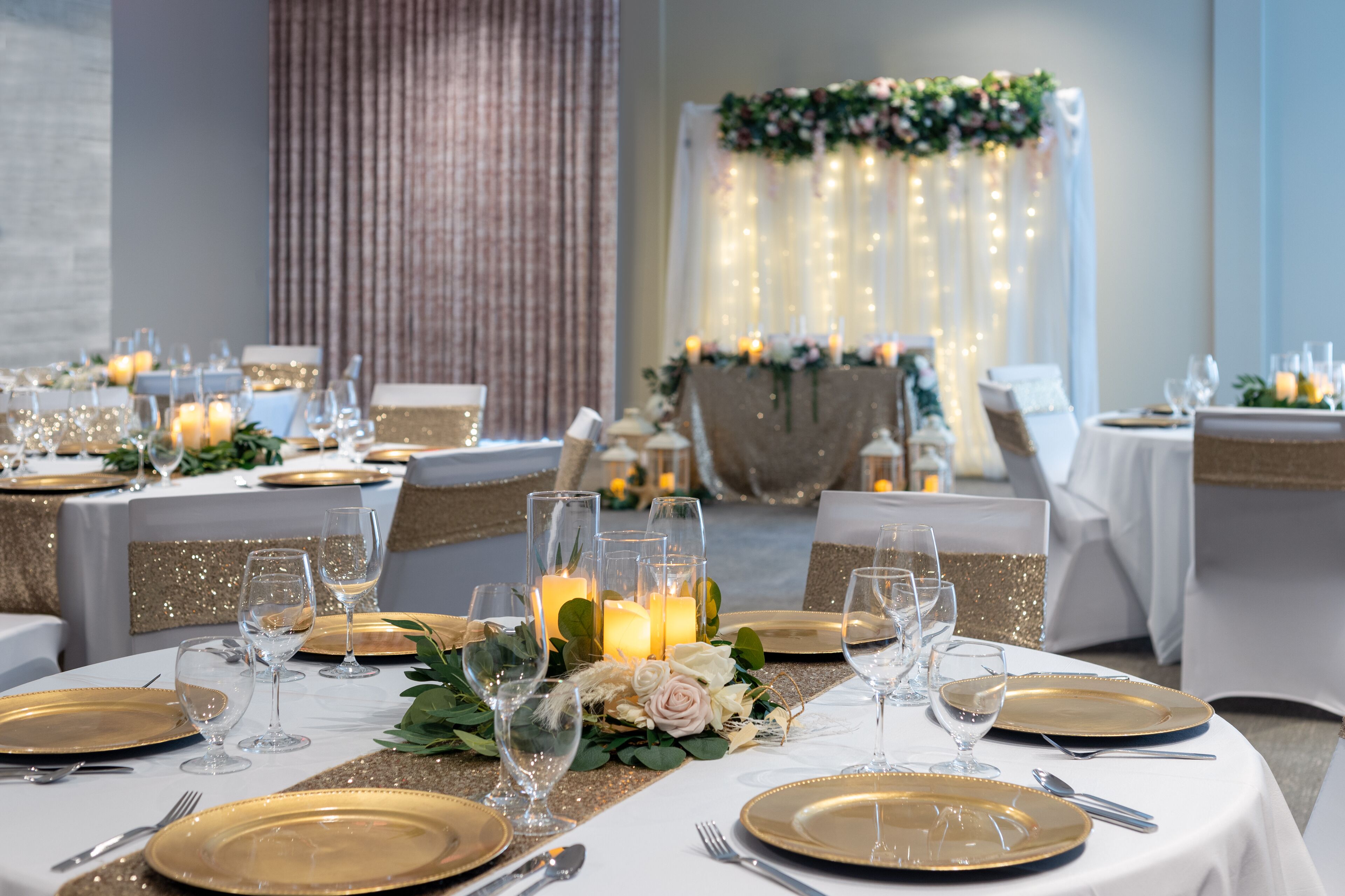 Une salle de banquet avec des tables rondes dressées pour un événement formel, agrémentée de décorations de table aux couleurs or et blanc, de bougies et de compositions florales.