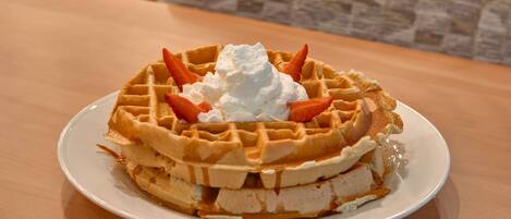 Un gaufre garnie de crème fouettée et de fraises, présentée sur une assiette blanche.