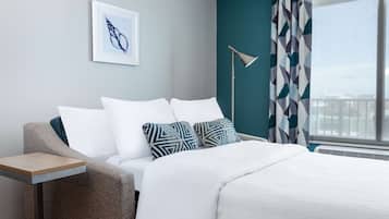 Una habitación de hotel moderna con cama, mesita auxiliar, lámpara de pie y ventana con cortinas.