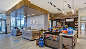 Ein moderner Empfangsbereich mit einem Holzbüro, einem Selbstbedienungs-Check-in-Terminal und einer Auswahl an Snacks und Getränken.