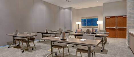 A conference room with multiple tables and chairs, equipped with laptops and glassware.