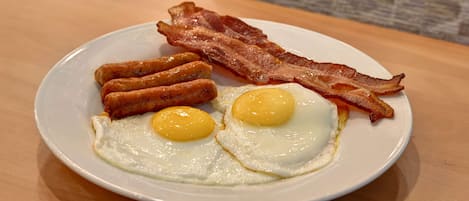 Un plato con dos huevos fritos, salchichas y tocino sobre un plato blanco.