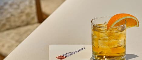 A glass of amber-colored beverage with ice and an orange slice garnish on a white surface. A napkin with the Hilton Garden Inn logo is visible.